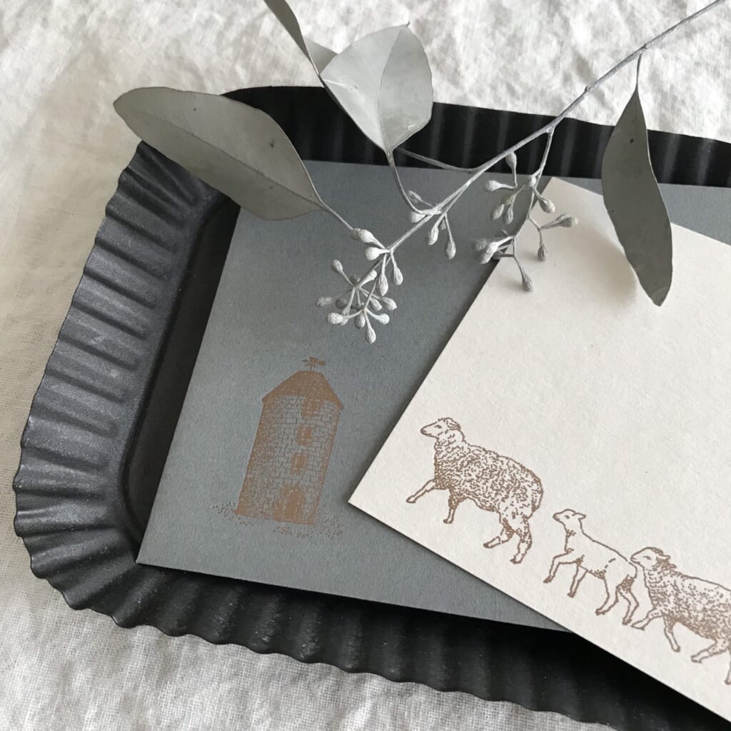 「ポストカード【羊を飼う】」羊飼いから届いたたよりのような羊だらけのポストカード。まきばのサイロには風見鶏ならぬ風見羊が春風に揺れるのを待っています。
